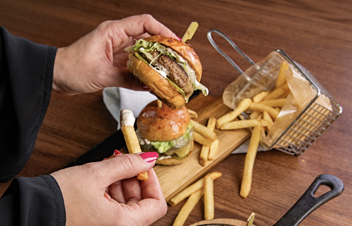 Person eating hamburger and fries. Image: Pexels - Denys Gromov