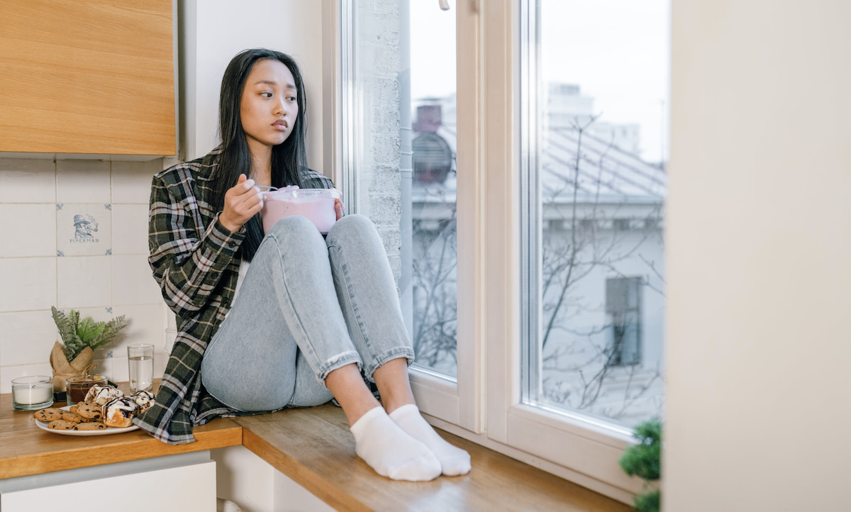 Female sitting on counter upset eating from tub of ice cream Image: Pexels - Alena Darmel