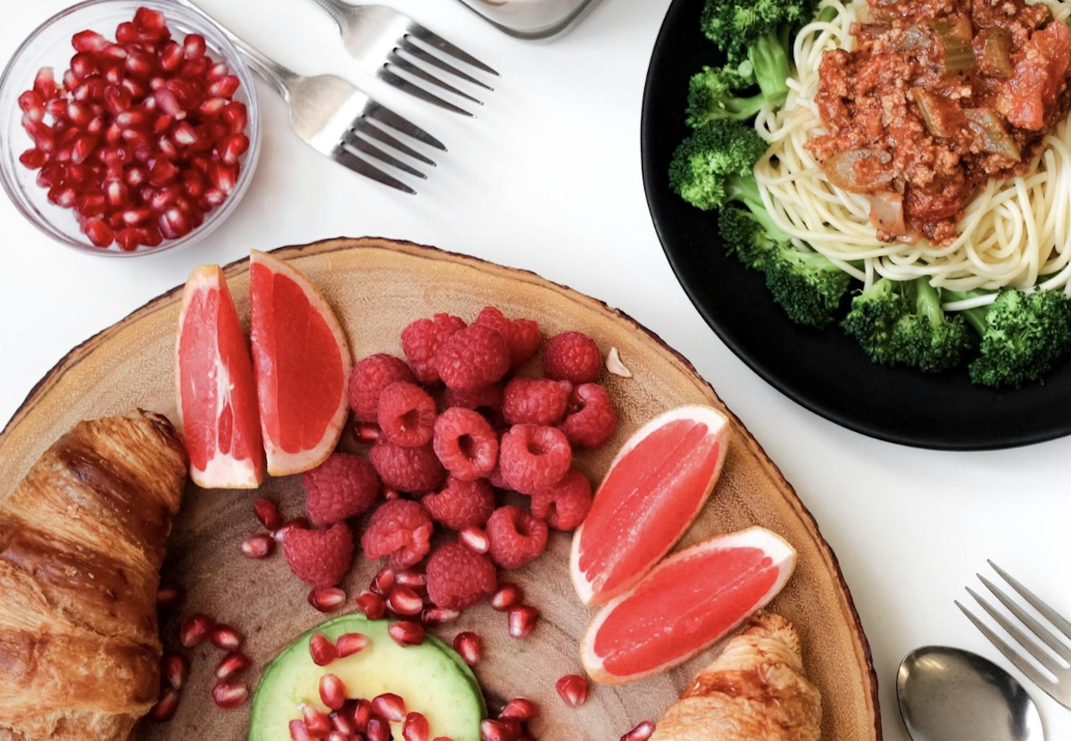 Food plated with croissants and fruit and then broccoli and pasta