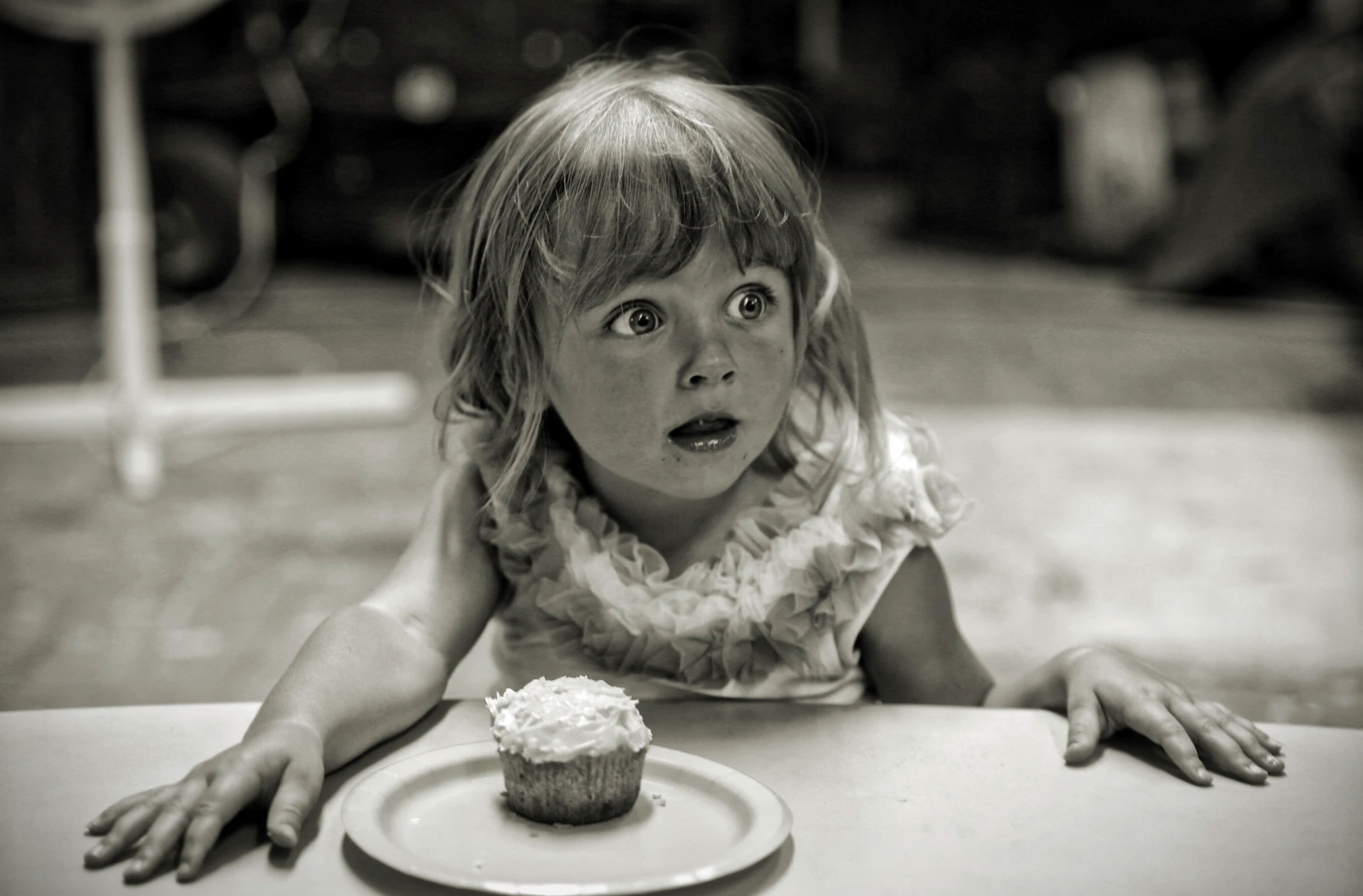Black and white photo with little girl sitting in front of a cupcake and surprised.