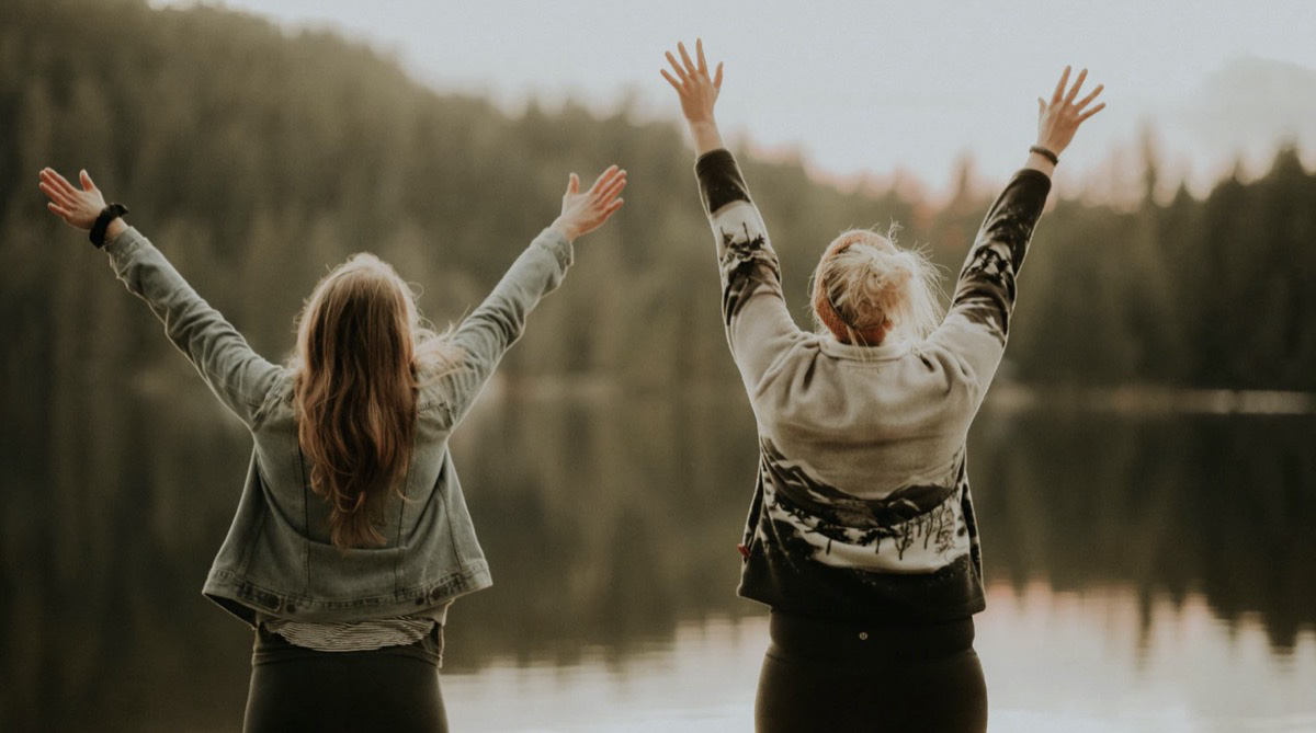 Girls excited and free at a lake in front of the mountains. Unsplash - Priscilla Du Preez