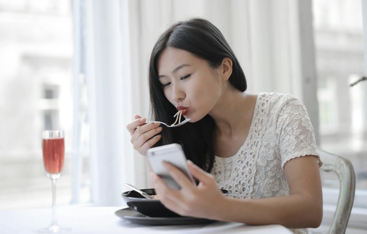 Woman eating while using phone. Image: Pexels - Andrea Piacquadio